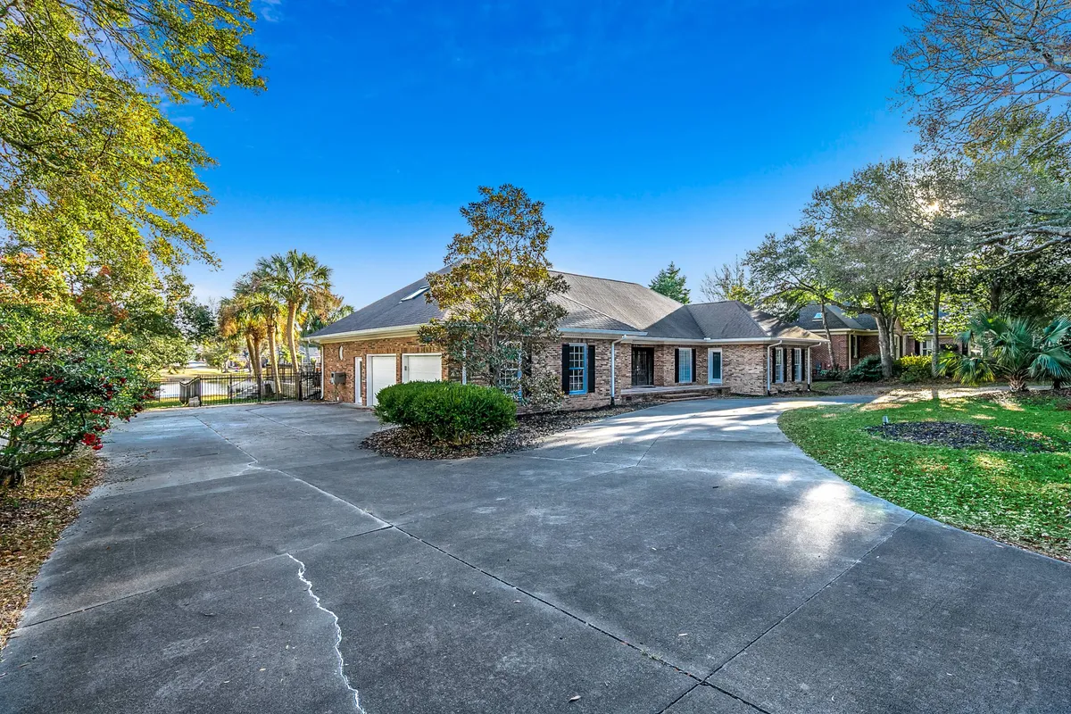 The main entrance of the house is shown with a welcoming driveway, lush greenery, and a tranquil front porch. The setting feels peaceful and inviting, suggesting a private, comfortable retreat just minutes from the beach.