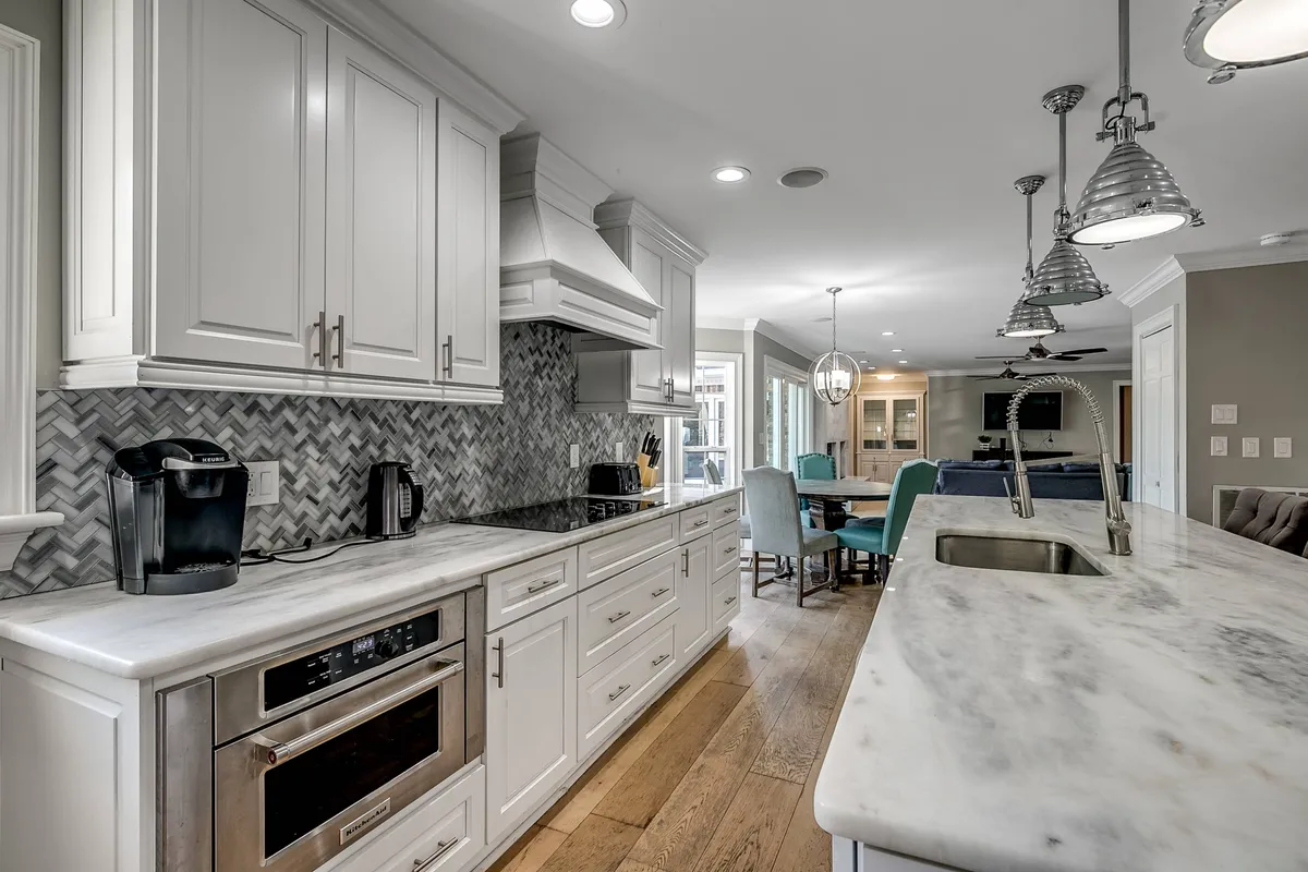 A contemporary kitchen featuring marble countertops, a stylish herringbone backsplash, a kitchen island with comfortable seating, and modern light fixtures. The open-plan layout hints at easy flow between the kitchen, dining, and living spaces.