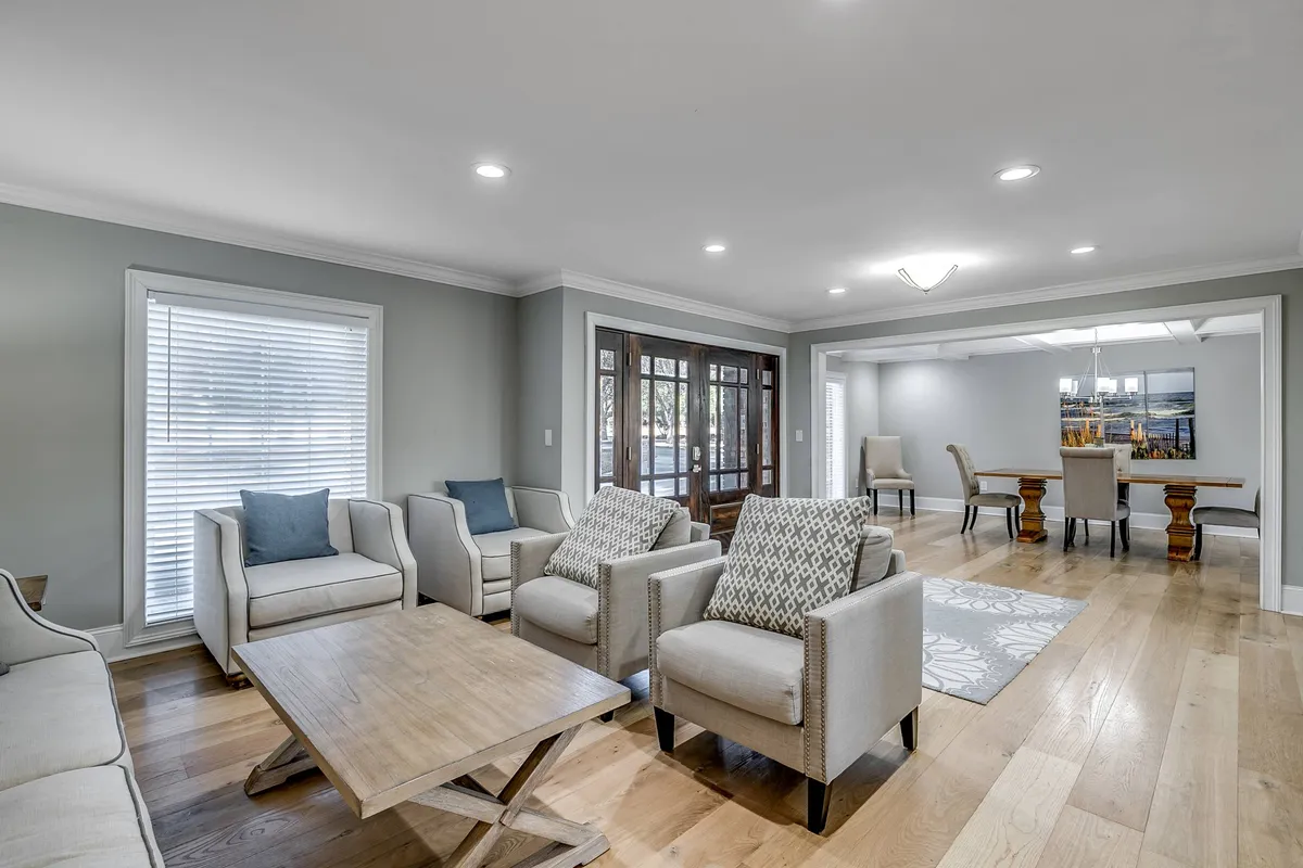 An inviting open-concept space featuring a comfortable seating area adjoining a wooden dining table with large windows streaming sunlight. The layout encourages seamless movement and interaction between the living and dining areas, capturing a sense of togetherness and warmth.