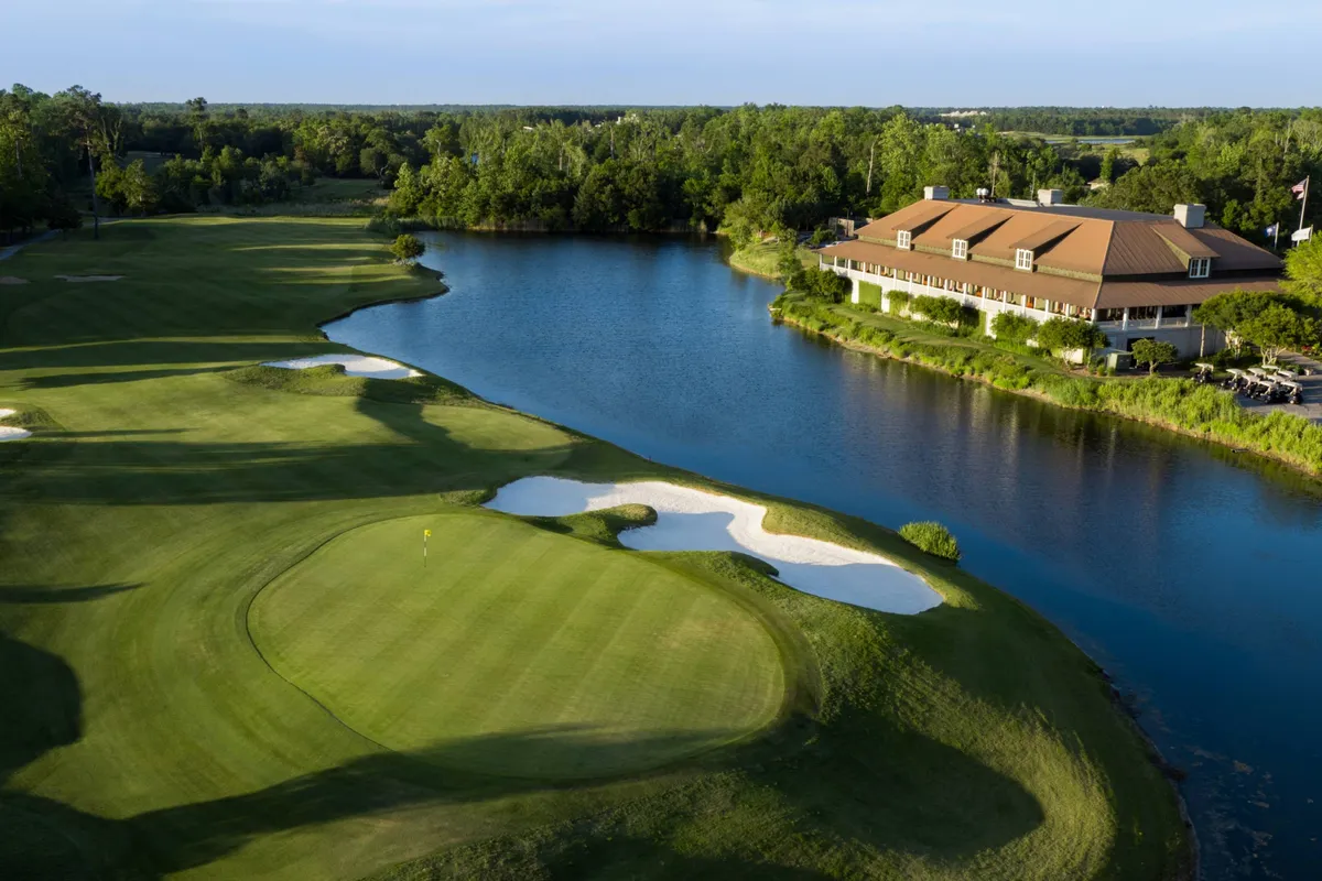 This image captures a lush golf course bordered by a serene lake, with a clubhouse in the background and sand traps adding to the sporting challenge. The scene conveys both the recreational and scenic aspects of the location, highlighting the opportunity for group golf outings in a beautiful, relaxing setting.