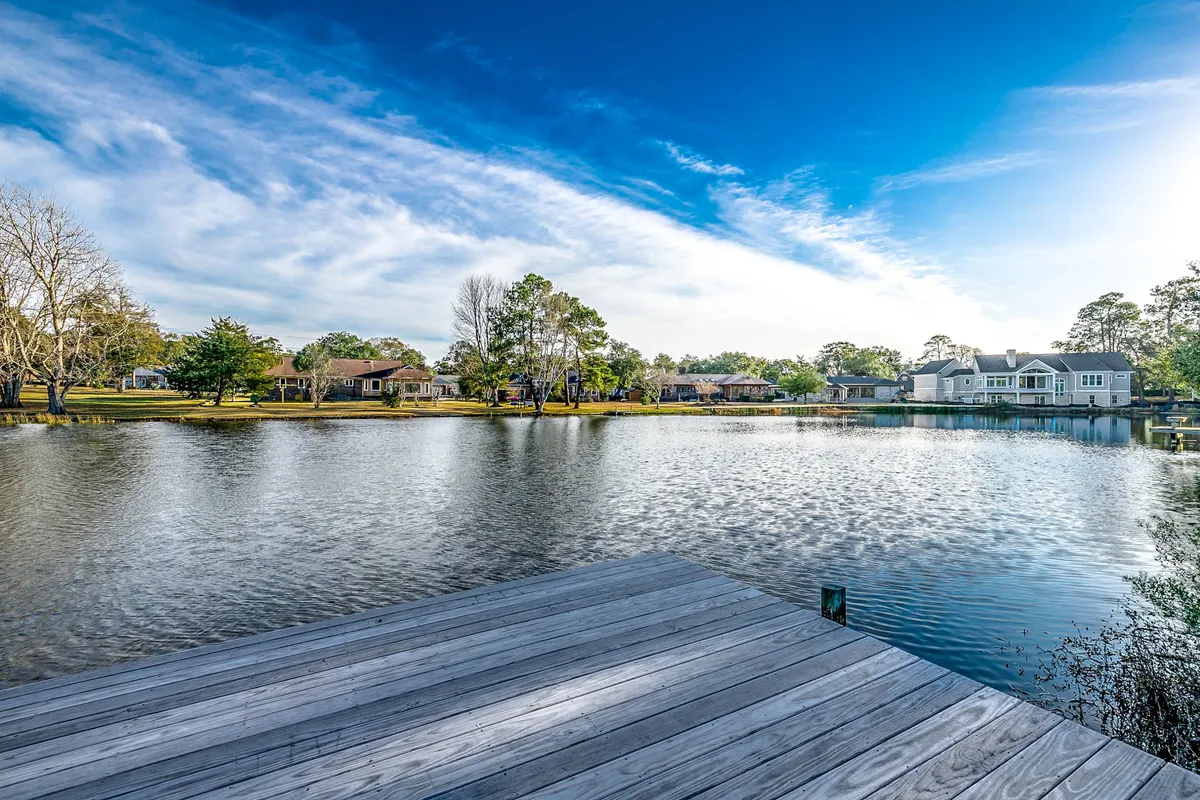 A tranquil view of a calm lake with a private dock jutting out into the water, surrounded by lush trees and waterfront homes. The scene is peaceful and inviting, ideal for fishing, boating, or simply enjoying the natural scenery. The sunset reflections on the water enhance the sense of a serene waterfront retreat.