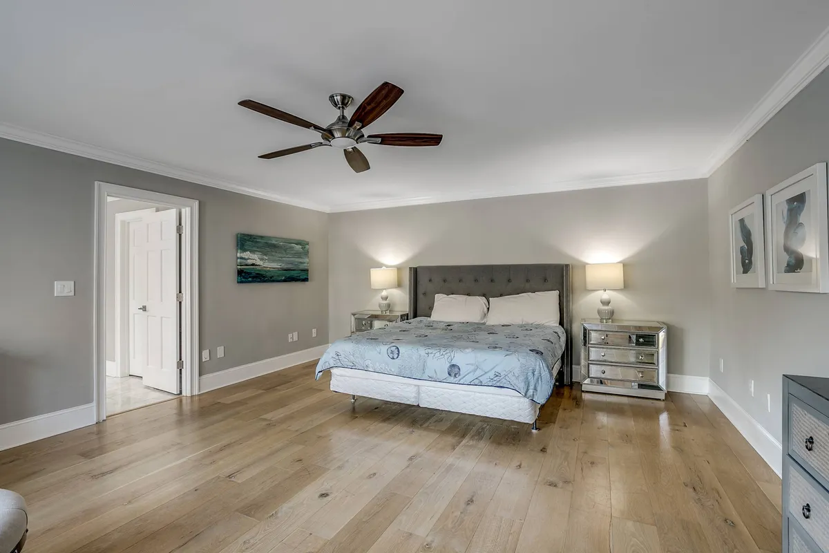 A tranquil bedroom with a bed flanked by nightstands, decorative artwork above the headboard, and a ceiling fan overhead. Warm natural light brightens the space, which feels peaceful and uncluttered.